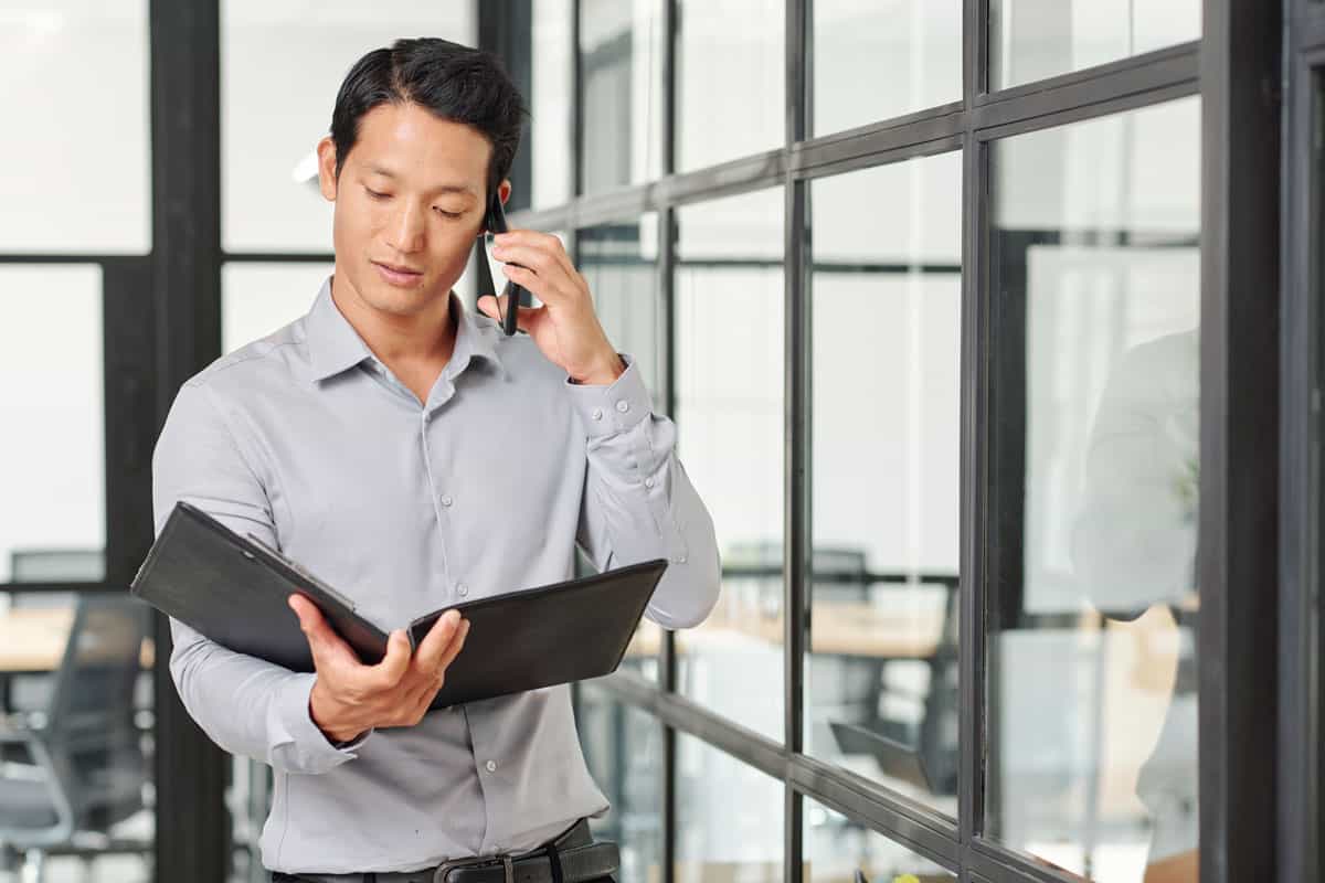 male auditor speaking on a mobile phone while reading corporate financial documents
