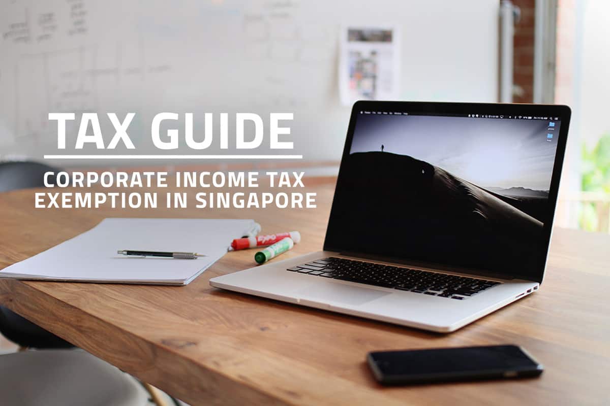 words tax guide corporate income tax exemption in Singapore overlaying background of notepad, laptop and mobile phone on a table in startup company meeting room