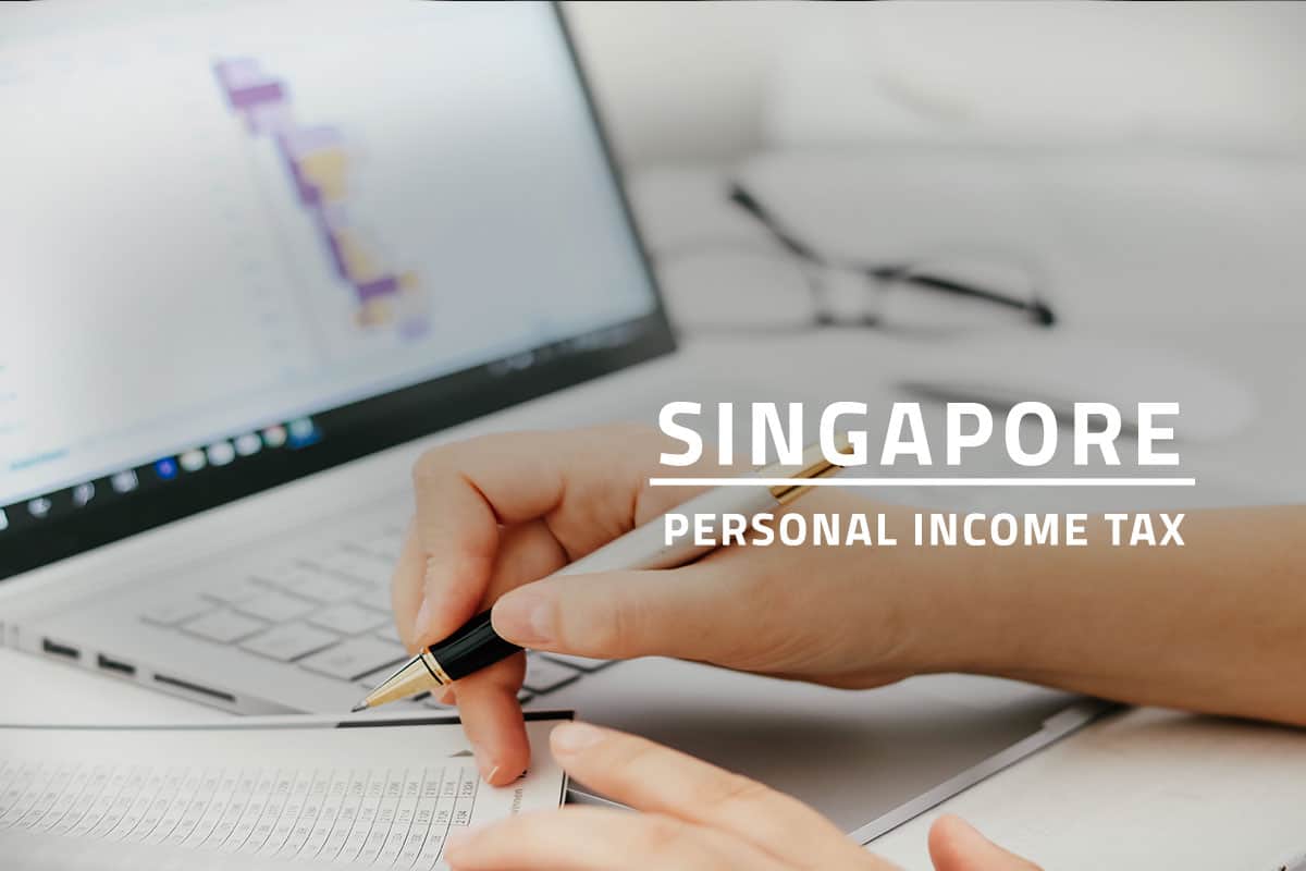 text Singapore personal income tax over background of an individual doing financial accounting. A hand is holding a pen, a printed financial report with a desk and a laptop in the background